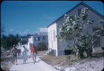 Four people and a dog walk on a path near houses in Great Guana Cay, Abaco, Bahamas
