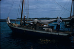 Sailboat crew folding mainsail while docked in Nassau Harbor, New Providence, Bahamas