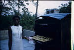 A Jamaican woman baking patties in an outdoor oven