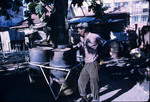 A steel pan maker standing next to empty steel drums in Trinidad