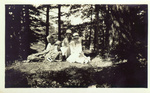 Black-and-white photograph of Alice Ellen and Clara Louise Guild, with two other women, sitting in forested area.