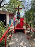 Gauchito Gil shrine in Parque Los Andes, Argentina, shows a statue with a cross surrounded by greenery and colorful walls by Wendy Howard