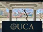 Students walk by the Universidad Catolica Argentina sign with vibrant trees in Puerto Madero under a clear sky by Wendy Howard