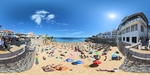 Visitors enjoying a sunny day at a popular beach in Lisbon, Portugal with umbrellas and activities along the shore by Wendy Howard