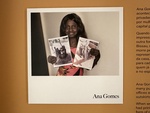 Woman holding photographs at a display in Lisbon, showcasing her connection to history and heritage by Wendy Howard