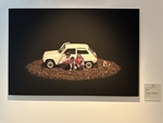 Artwork featuring a white car surrounded by children sitting amidst wood chips in Lisbon art gallery by Wendy Howard